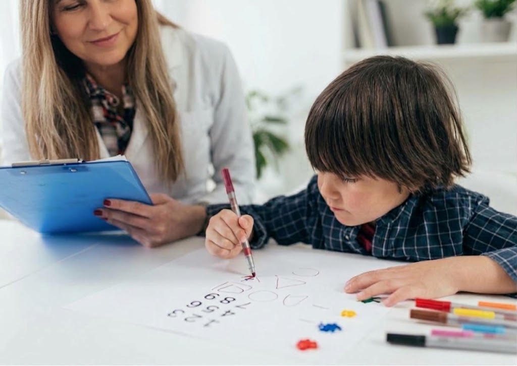 Criança desenhando formas e números em uma folha enquanto a psicóloga acompanha com uma prancheta