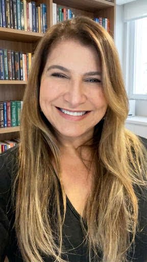 Retrato de Christina Faria, sorrindo, diante de uma estante de livros